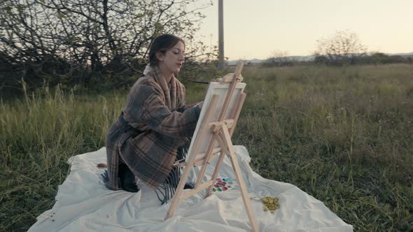 Young girl paints a picture sitting on the grass