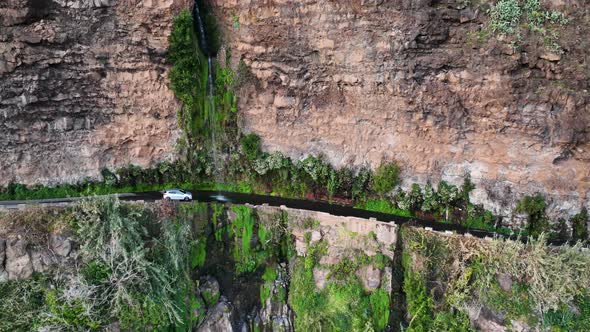 White car drives under Angels waterfall that cascades onto cliffside road; drone