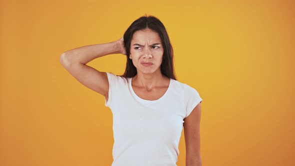 Thoughtful and Disappointed Woman is Scratching Her Head Shrugging Shoulders Over Orange Background