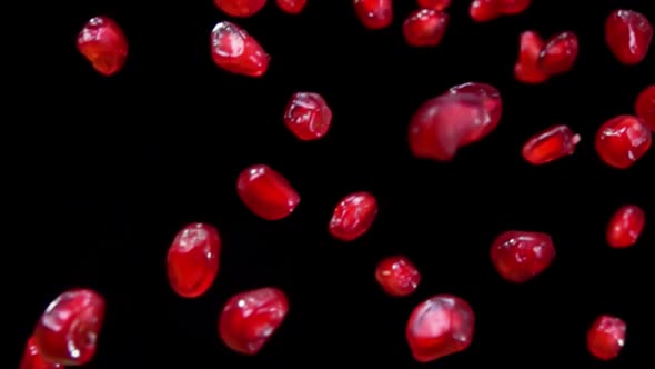 Red Juicy Ripe Pomegranate Grains Are Falling Diagonally on the Black Background