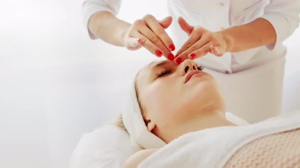 Beautician cosmetologist makes face massage and applies a moisturizer cream