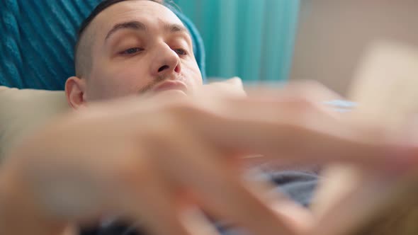 A Man is Reading a Book Lying on the Couch at Home Soft Focus