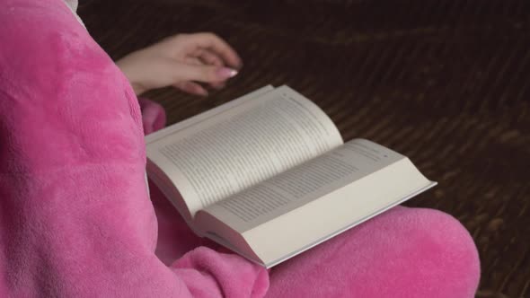 Young Woman in Pink Pajamas Sitting Reads a Book