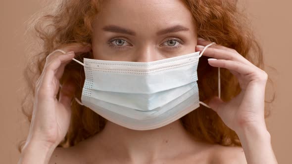 Woman Putting On Protective Face Mask Posing Over Beige Background