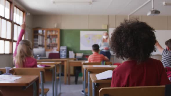 Group of kids wearing face mask raising their hands in the class at school