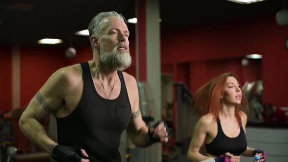 A gray-haired adult man runs on a treadmill next to a young woman