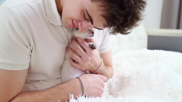 a Young Man Holds a Small White Kitten and Kisses Him