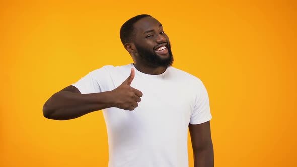 Young Bearded Black Guy Giving Thumbs Up, Smiling at Camera on Yellow Background