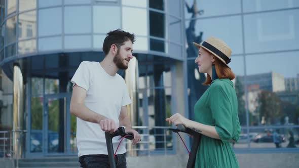 Admiring Couple in Love Looking Around When Standing on Electric Scooters