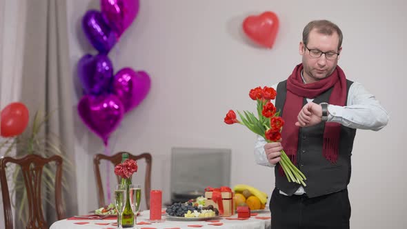 Worried Caucasian Husband Waiting for Wife on Valentine's Day with Bouquet of Tulips at Decorated