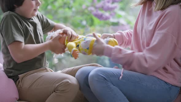 Side View Unrecognizable Teenage Girl Fighting for Doll with Little Boy Sitting on Windowsill