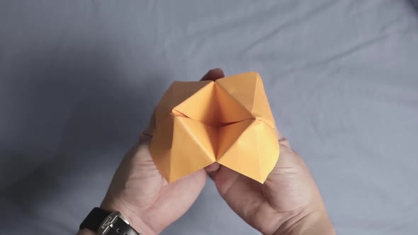 Close-up on Hands Playing with Orange Folded Paper Fortune Teller Origami