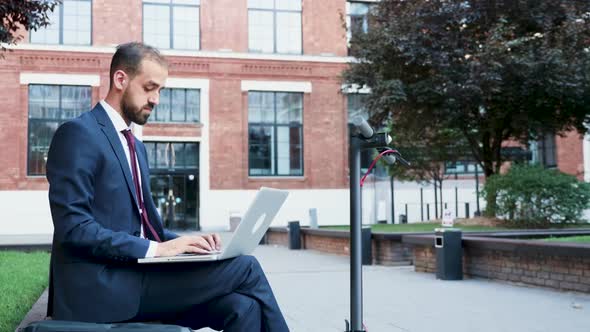 Businessman Outdoor Typing on the Laptop Sitting in a Business District