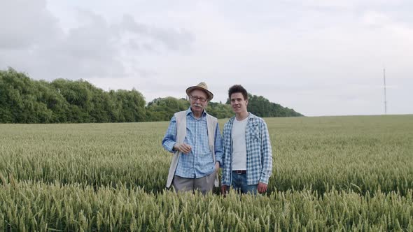 Two Farmers of Different Ages Talking Gesturing with Joy in a Wheat Field