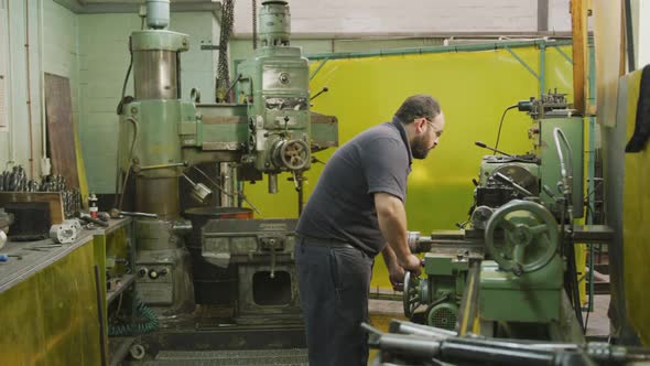 Caucasian male factory worker at a factory sitting at a workbench and operating machinery