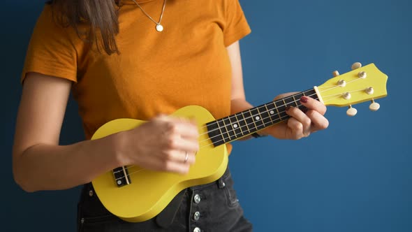 Woman in T-shirt Plays Ukulele Standing Near Blue Wall