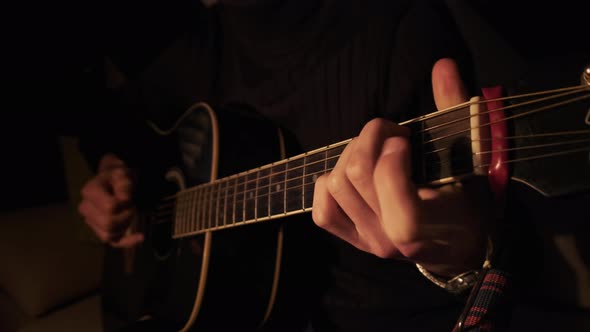 Man Playing Acoustic Guitar at Home in Atmospheric Dark Warm Lighting