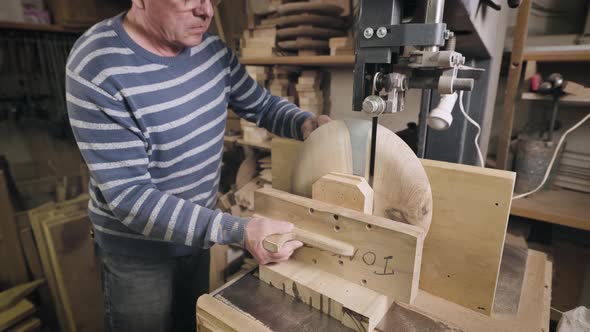 An Elderly Man in a Carpentry Workshop Saws Off the Remains of a Wooden Workpiece