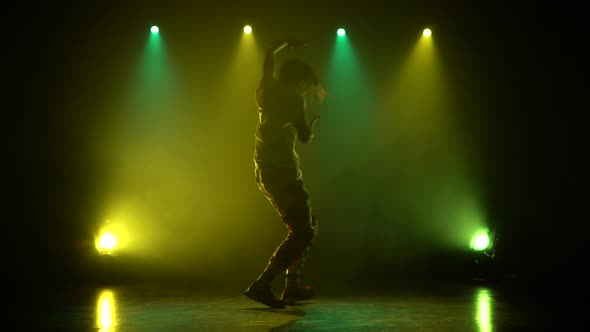 Man Enjoying Hip Hop Moves in Dark Studio with Smoke, Green and Yellow Lighting. Silhouette