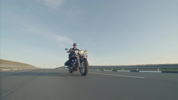 Man in Helmet and Glasses on Motorbike Rides Along the Highway Background Sky and Approaches the