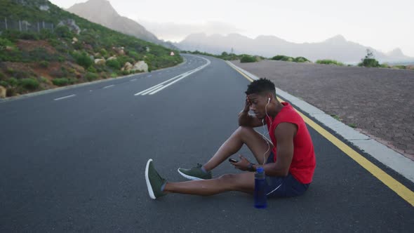 African american man holding smartphone taking a break from running on the road