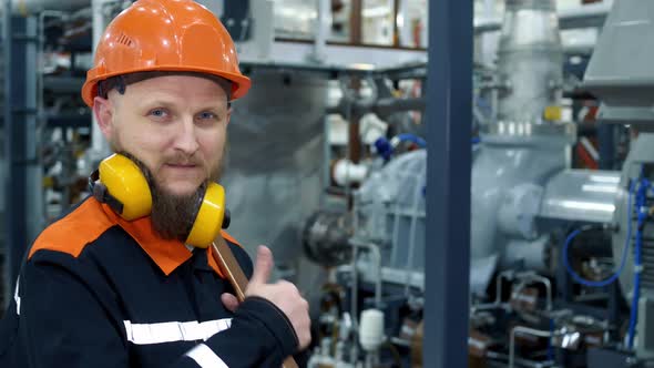 A Plant Worker in Headphones and a Helmet with a Wrench at His Workplace a Technological Compressor