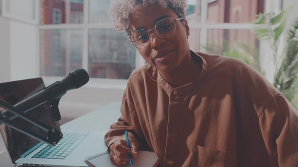 Young African American Woman Radio Host in Headphones Sits at Desk with Laptop