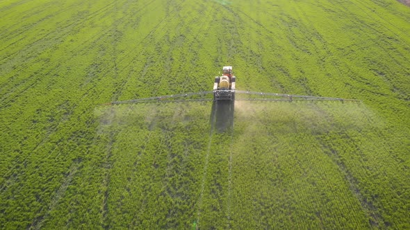 Aerial View of Farming Tractor Spraying on Field with Sprayer, Herbicides and Pesticides at Sunset