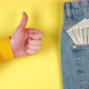 Female hand showing thumbs up against a background of many dollars in a jeans pocket - VideoHive Item for Sale