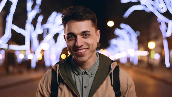 Portrait of Joyful Handsome Man 20s Smiling While Strolling in Evening City Across Main Avenue with