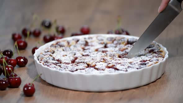 Cutting clafoutis with cherry in ceramic form