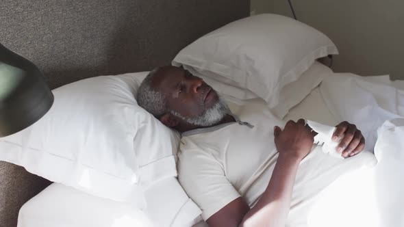 Sick senior african american man couching while lying on the bed at home