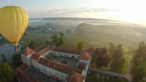 Colorful Hot Air Balloons Fly Over the Medieval Castle and Lake in the Morning Fog. Maneuverable