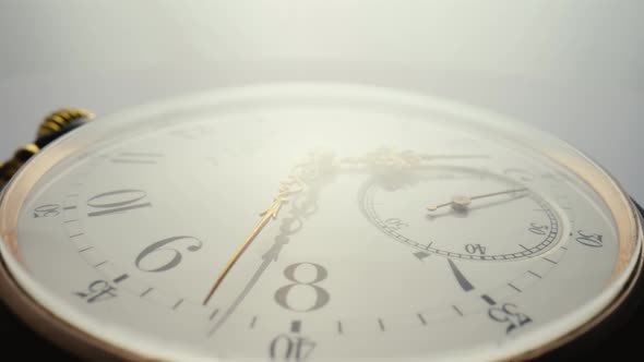 Antique Pocket Watch with a White Dial and Gold Moving Hands is Spinning in Bright Light