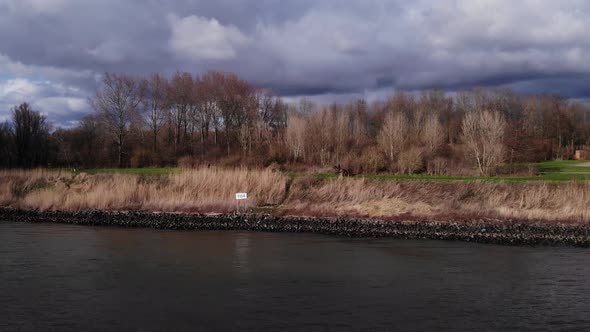 Person Horseback Riding By The Calm River Of Oude Maas Near Countryside Of Puttershoek, Netherlands.