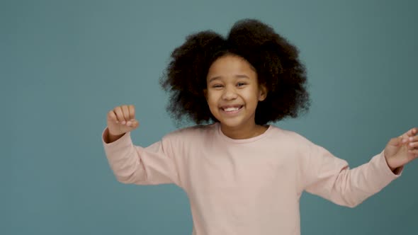 Portrait of cheerful little girl with curly hair smiling funny and dancing joyfully