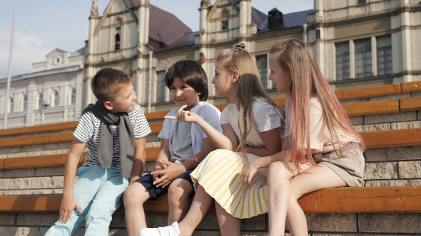 Four cute friends kids talking sitting on a bench.