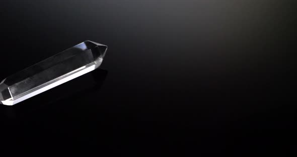 A clear see through crystal with light shining isolated on a black mirror background SLIDE LEFT.