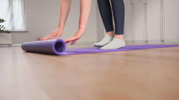 Woman spreading yoga mat after training in studio. Girl folding fitness mat on floor at yoga studio