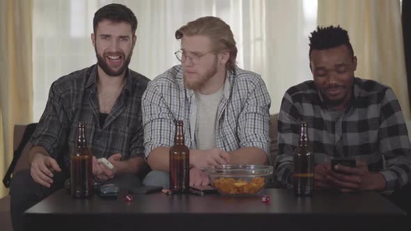 Three Happy Men Friends Sitting at House on the Cauch, Looking Tv, Drinking Beer with Chips, Having