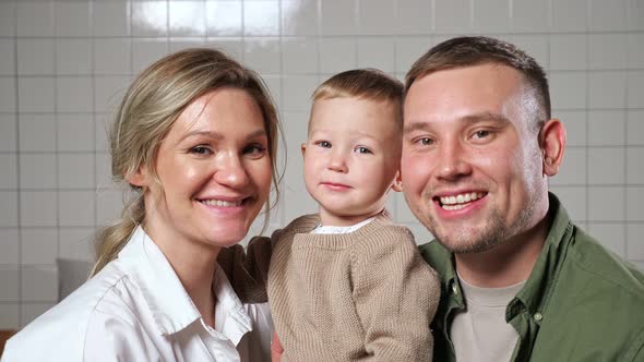 Parents Hold Little Son in Arms Standing Against Wall