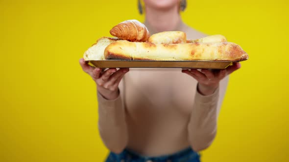 Unrecognizable Young Caucasian Woman Holding Tray with Ciabatta and Croissants Standing at Yellow