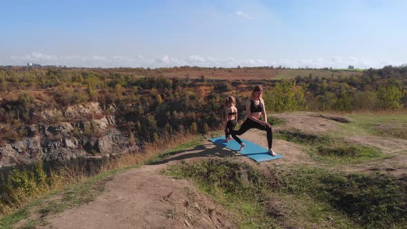 Aerial Drone View of Slender Young Mother Do Yoga Exercises with Child Daughter on High Hill By Lake