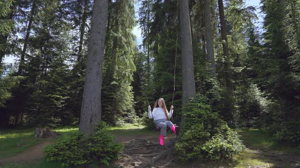 Girl on Swing Between Trees in Forest