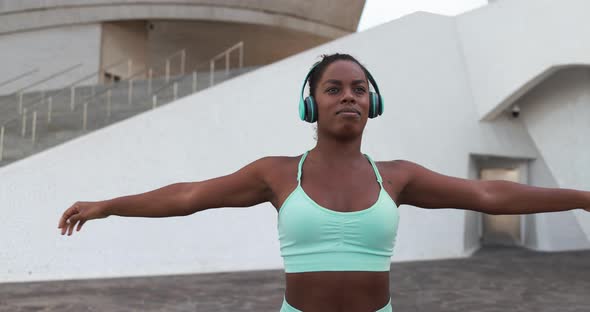 Fit young african woman doing sport stretching workout in the city while listening music playlist