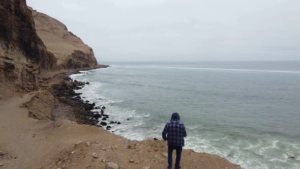 Drone video of a person running towards the edge of a cliff by the ocean rocky shore. Drone flies ov