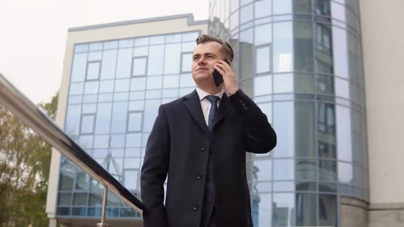 Young Elegant Businessman Talking on Phone Near the Office Center