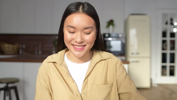 Intelligent Asian Female Looking at Camera Sitting at the Desk in Front of Laptop