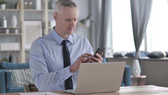 Gray Hair Businessman Using Smartphone at Workplace