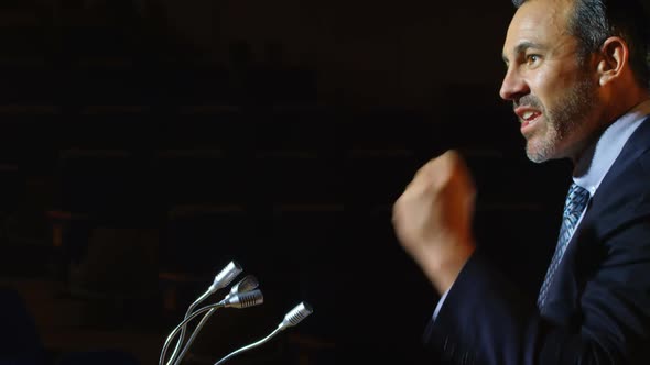 Caucasian businessman speaking at podium on stage in auditorium 4k